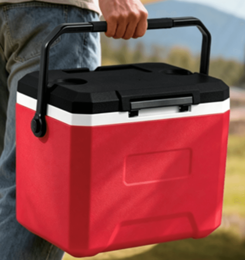 A person carrying a red and black portable cooler with a sturdy black handle outdoors.