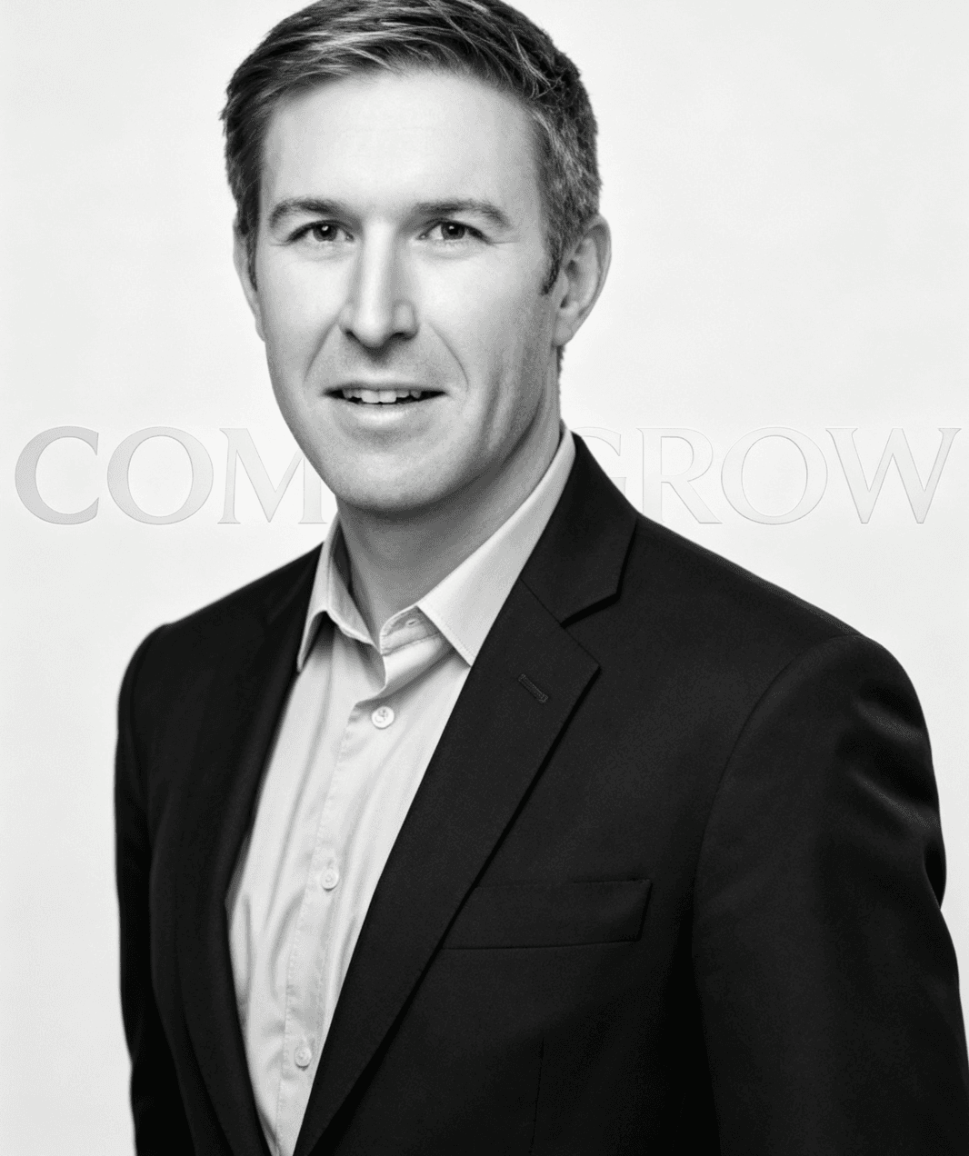 Black and white professional headshot of a man wearing a dark suit and collared shirt.