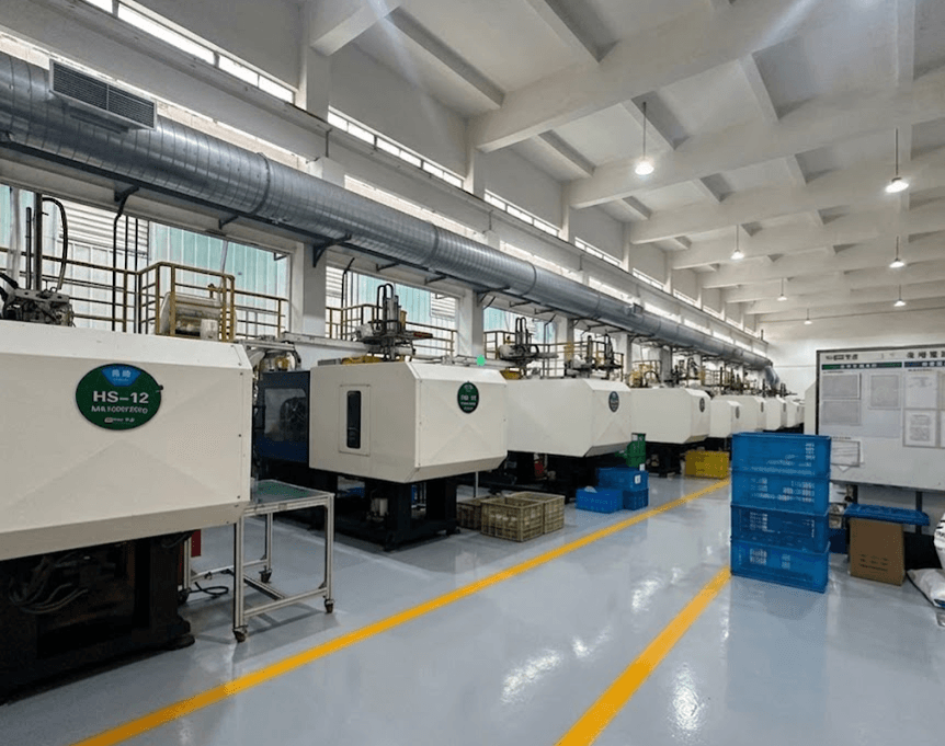 Row of white injection molding machines in a clean factory with yellow floor markings.